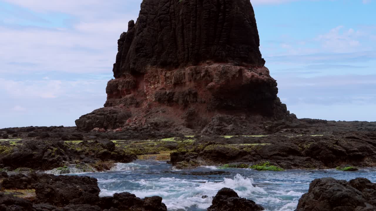 A camera tilts up to reveal the majestic standing rock, towering above its surroundings against a clear sky, capturing its natural grandeur.