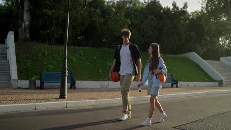 young couple walking together in a park holding basketballs