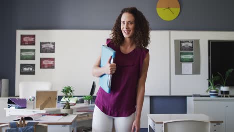 video of happy caucasian female teacher standing in classroom and holding book