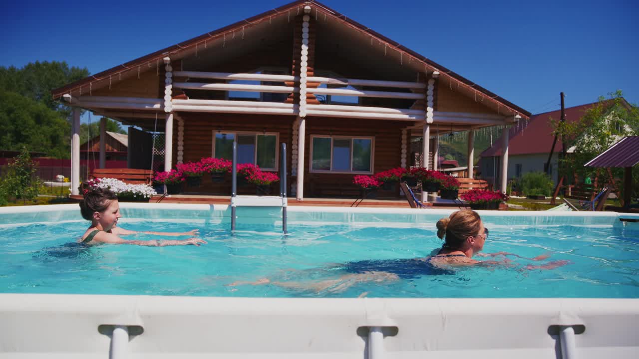 Kvinde og pige svømmer i udendørs pool foran et træhus