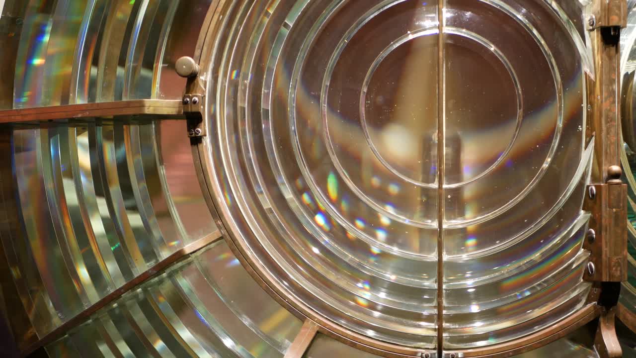 Fresnel lens with brass structure, nautical lighthouse tower. Detail of the glass lantern with rainbow spectrum. System of lamps and lenses to serve as a navigational aid. Old sea searchlight beacon.
