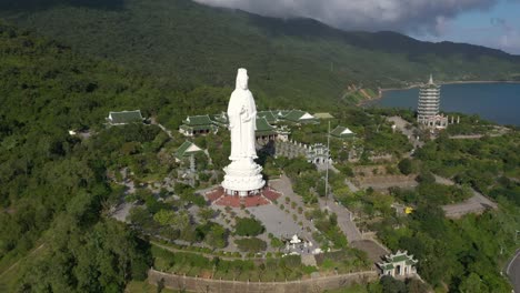 close aerial of tall lady buddha statue and temples with huge mountains and ocean in da nang, vietnam