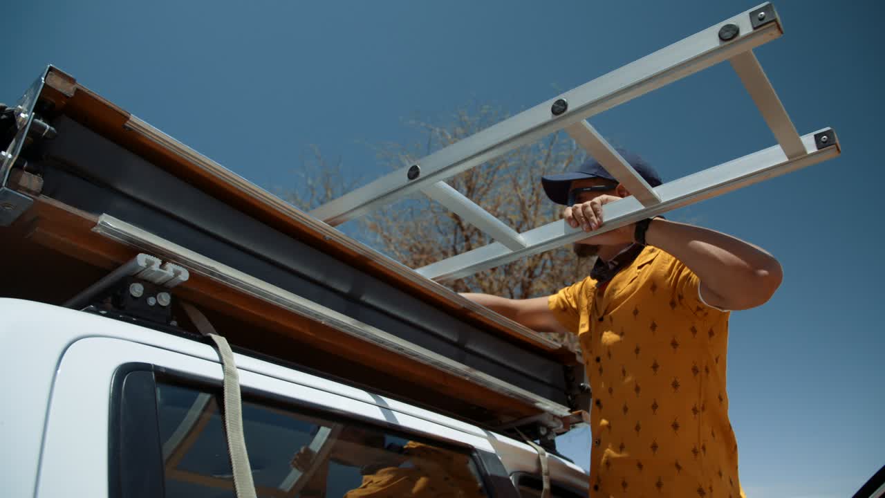 Handheld shot of a tourist standing on his off road vehicle, pulling out the ladder of his canvas rooftop tent and inspecting it in Africa.
