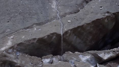 Water-stream-flowing-down-the-melting-glacier-covered-with-dirt-in-Caucasus,-Georgia