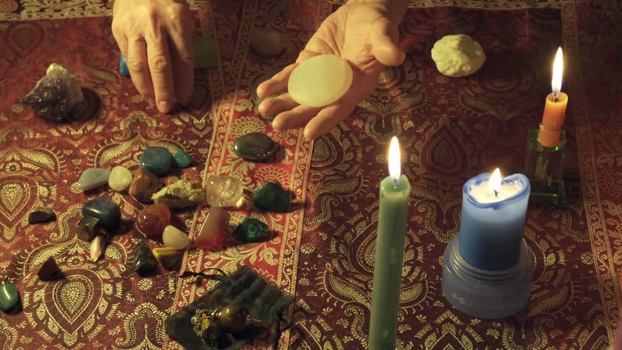 primer plano de manos realizando rituales alternativos con gemas mágicas en una mesa mística con piedras curativas y velas
