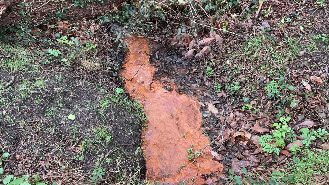 Stream polluted with bright orange running down stream.