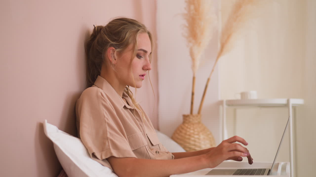 Young freelancer woman works on laptop in bed at home