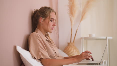 young freelancer woman works on laptop in bed at home