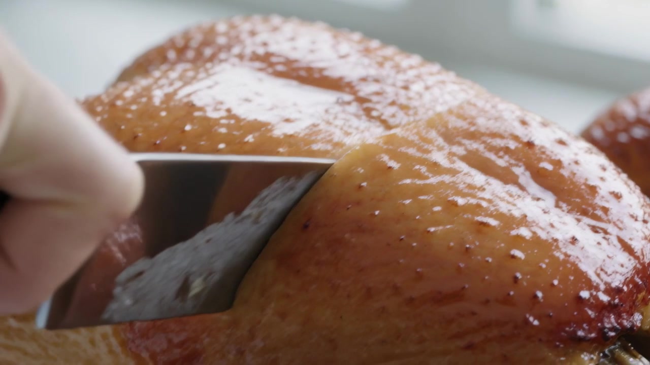 Mano che intaglia, premendo un coltello di metallo, affetta pollo arrosto su un bancone vicino alla finestra, pronto per essere servito.