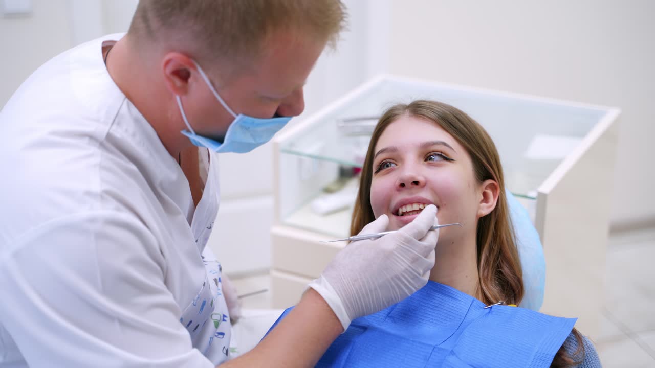 Beautiful woman with opened mouth at stomatologist. Professional dentist looks at patient's teeth using medical instrument in clinic.