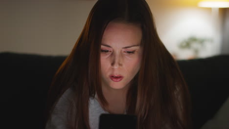 Close-Up-Of-Anxious-Woman-Sitting-On-Sofa-At-Home-At-Night-Looking-At-Mobile-Phone-Concerned-About-Social-Media-Or-Bad-News-1