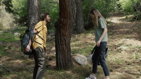 Caucasian-couple-hiking-with-backpacks,-stop-to-take-a-rest-under-the-tree