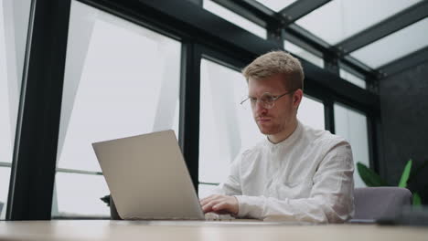 handsome man is working with laptop in modern office in daytime person in white shirt is surfing internet