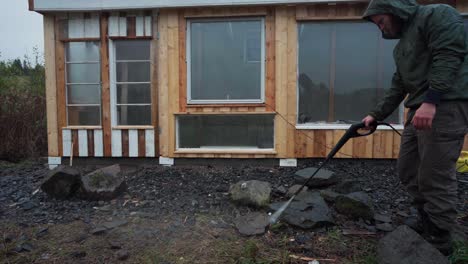 a man is utilizing a pressure hose to clean the rocks surrounding the greenhouse in indre fosen, norway - close up