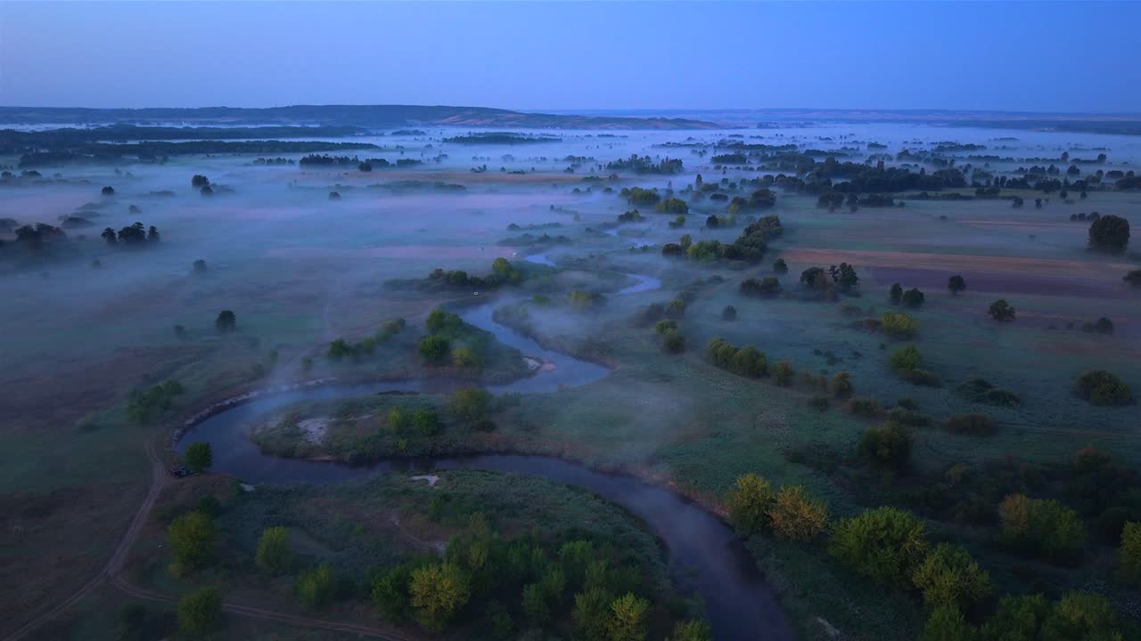 Misty morning over Nida river, Poland, with trees and fields, aerial view