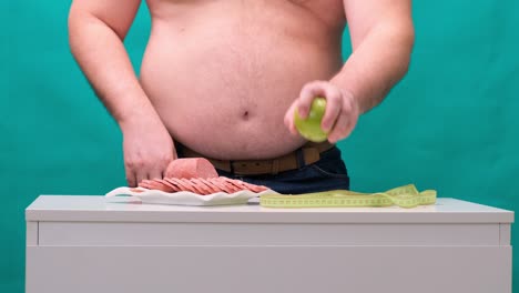 man with a fat belly chooses between sausage and a green apple. the concept of diet and willpower