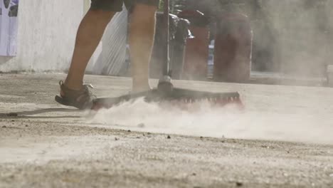 a man sweeps the ground with a red push broom in palau