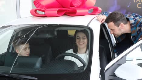 a young family with children inspecting a new car and talking to a dealer at a dealership. a husband and wife are looking at a new luxury model of an electric car. technology and people concept