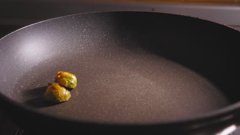 a close up shot of the hand of a chef as he carefully places his freshly sliced and marinated brussels sprouts onto the surface of a hot non stick frying pan to roast