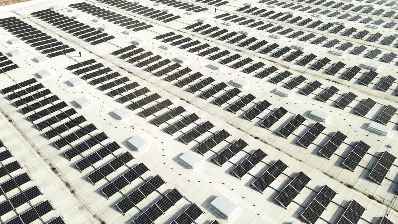 Veduta aerea di pannelli solari per energia rinnovabile sul tetto di un edificio industriale o un magazzino durante una giornata di sole primaverile con un po' di neve bianca e soffice che si scioglie sotto di essi.