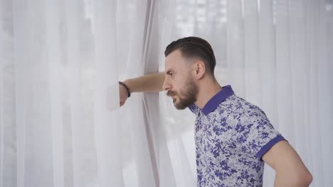 Thoughtful-and-depressed-man-looking-out-window-at-home-and-feeling-bored.