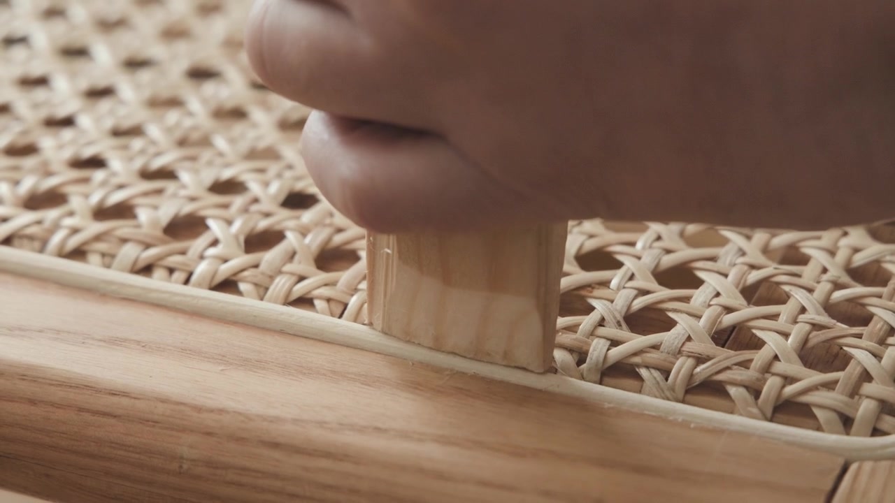 Restauro di una sedia in rattan, un artigiano sta martellando il listello nella sua posizione sulla struttura della sedia.