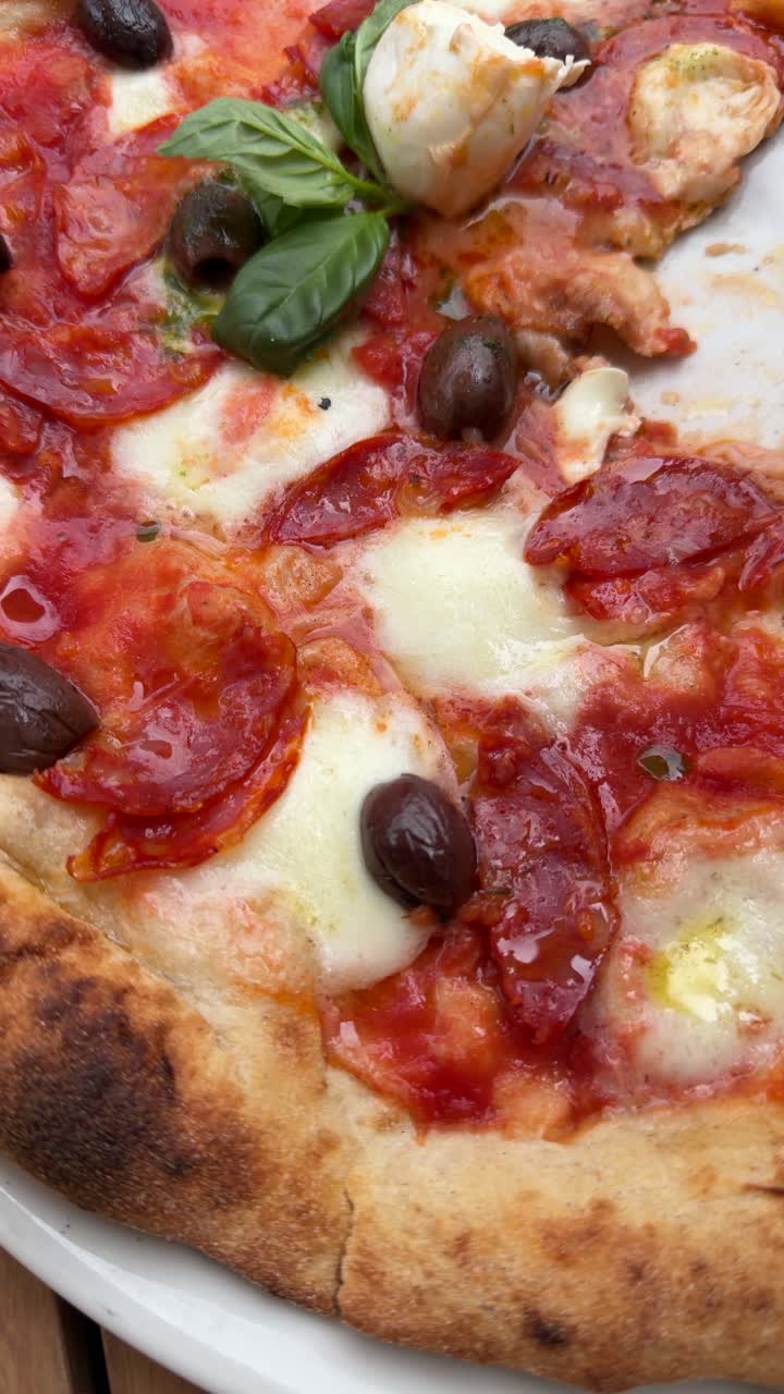 Primo piano di una deliziosa pizza con salame piccante, olive e basilico