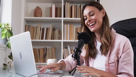 woman recording podcast at home, using laptop and microphone, smiling warmly