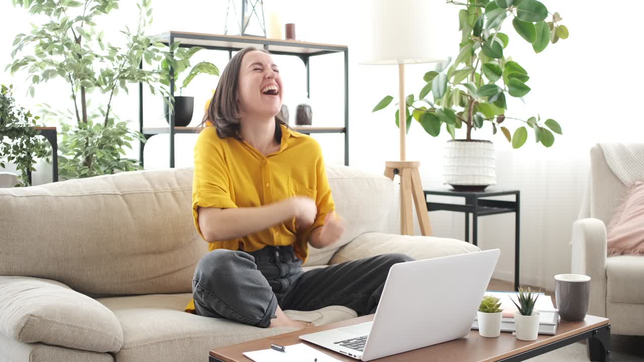 Excited woman dancing on sofa while working from home