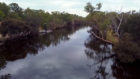 Aerial-moving-forward-over-a-narrow-calm-river-with-trees-either-side