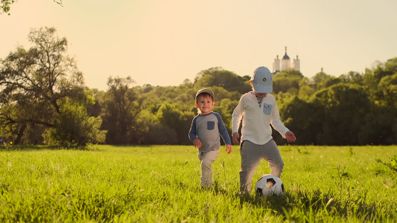 dos niños pequeños jugando con una pelota de fútbol riendo y sonriendo al atardecer.