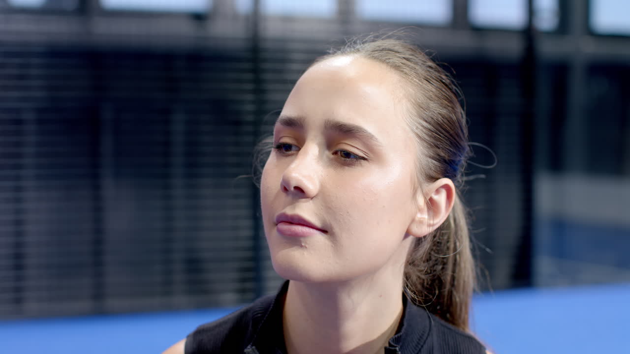 Young woman focused and determined on padel tennis on indoor court, ready for action, copy space