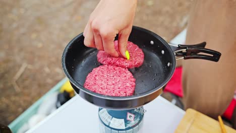 fresh patties hit the pan as camping cooking begins over portable gas stove