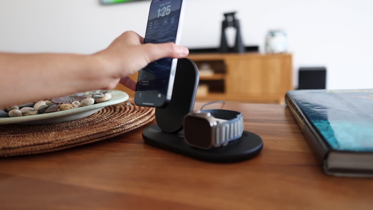 A hand interacts with a wireless charging station, placing and removing a smartphone in a modern, well-lit room
