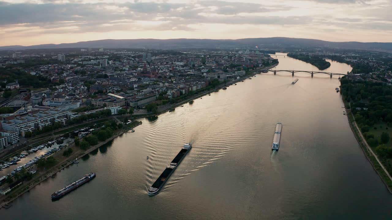 Summer Sunset over Mainz approaching the Dom with the Rhine river with cargo ships and reflections on the water and old bridge in the background