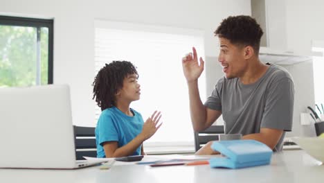 Hombre-Birracial-Feliz-Y-Su-Hijo-Haciendo-La-Tarea-Juntos,-Chocando-Los-Dedos