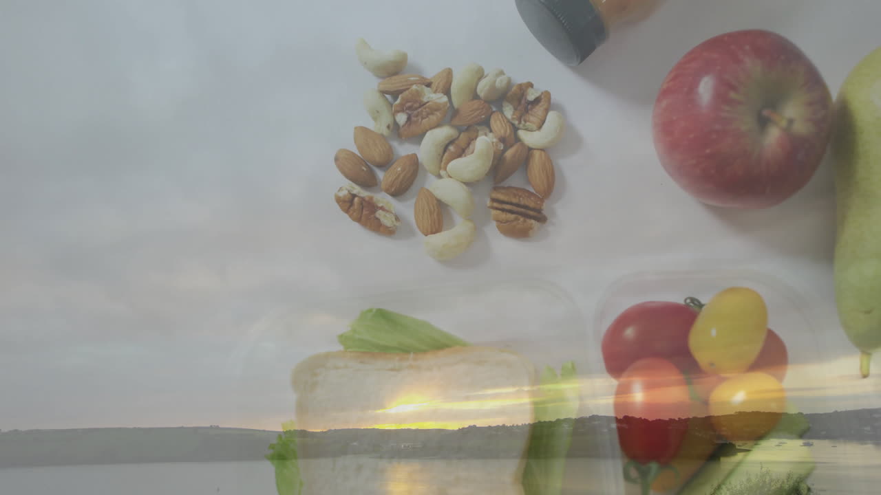 Over serene lake landscape at sunset, nuts, fruits, and sandwich displayed
