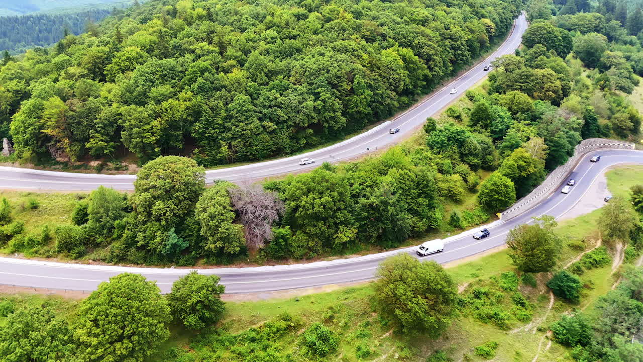 Winding road through lush green hills. Curved highway snakes through dense greenery, showing vehicles traveling on a beautiful sunny day in nature