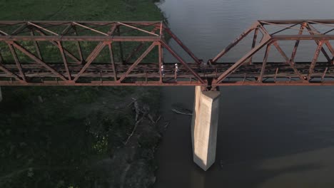 aerial tracks people walking across river on abandoned railway bridge