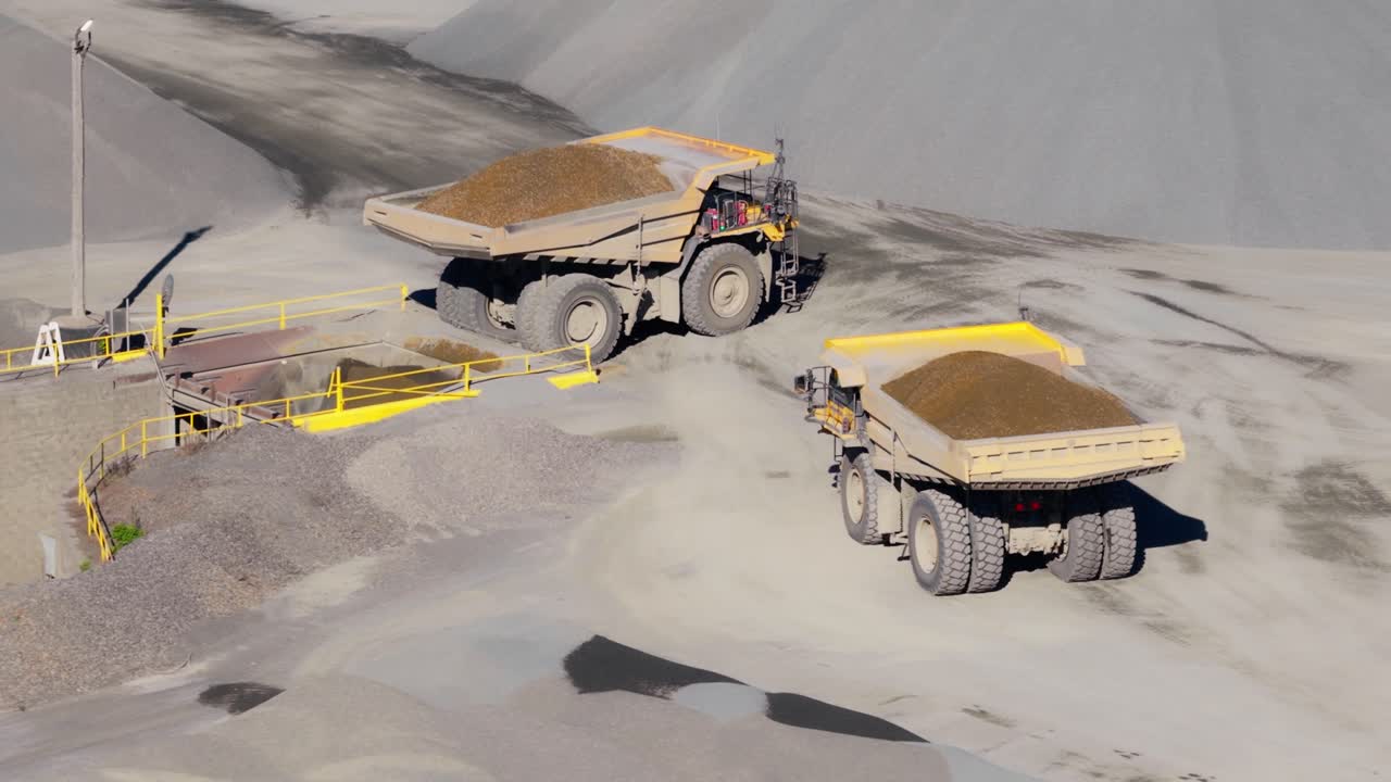 Large haul trucks transporting aggregate inside open pit quarry, parked waiting, medium aerial pullback