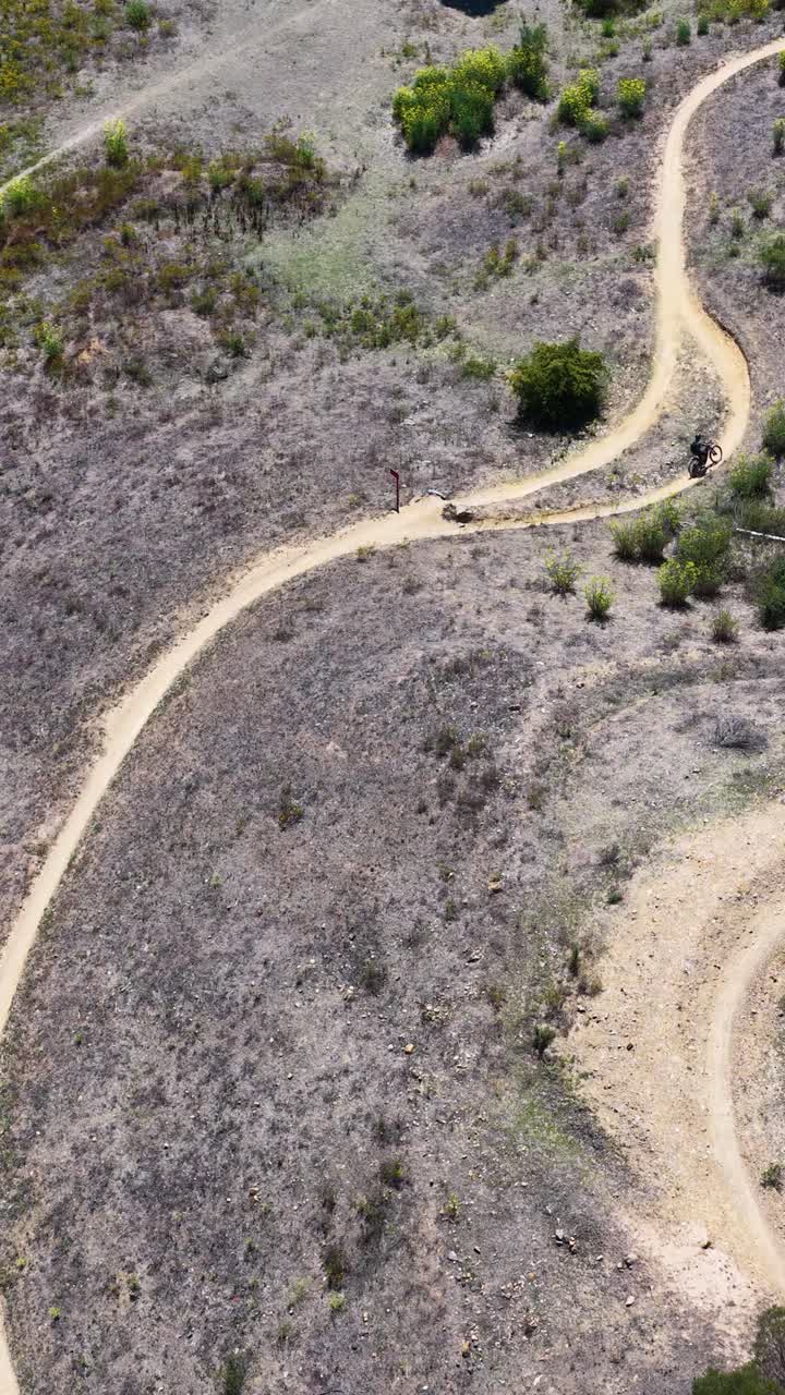 Ripresa aerea con drone di un ciclista che percorre un sentiero sterrato curvo attraverso la boscaglia australiana