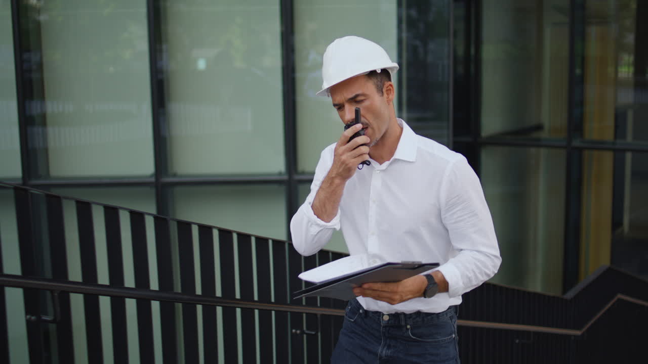 Hardhat engineer going upstairs dictating message at city closeup. Man talking