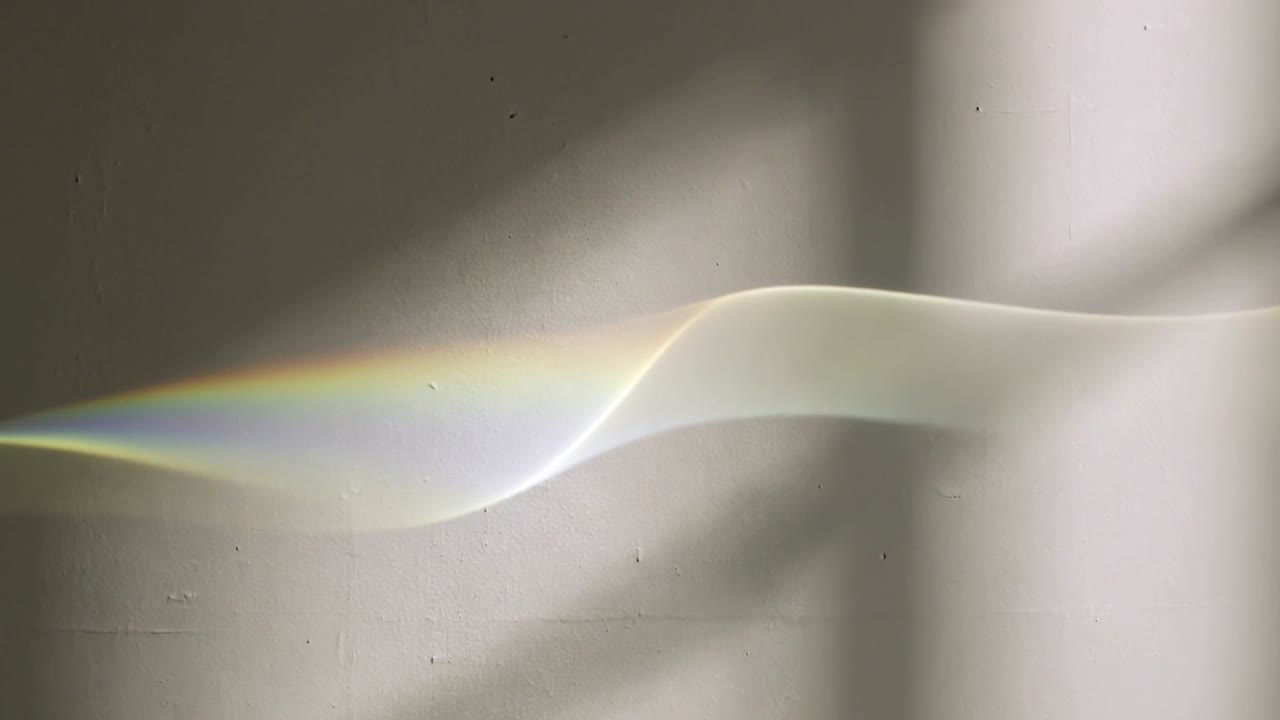 Shifting thin refracted light band moving rightward across pale wall, sunlight passing curved glass