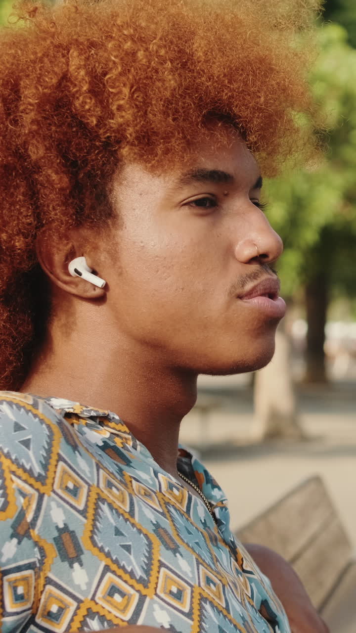 Giovane uomo dai capelli rossi e ricci che ascolta musica con gli auricolari