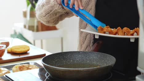 young woman frying sausages using tongs on hot pan at home, the process of making a burger complementary