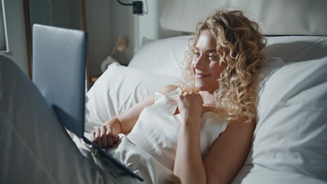 smiling lady surfing laptop in home bed. joyful girl lying watching social media