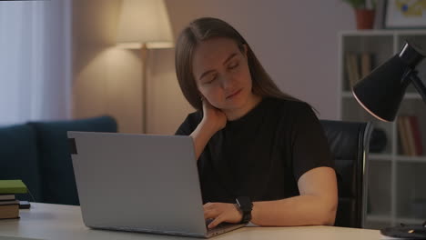 mujer cansada con dolor de cuello y osteocondrosis está escribiendo en el teclado de la computadora portátil trabajando en casa por la noche enfermedad de la columna vertebral y cansancio del trabajo informático