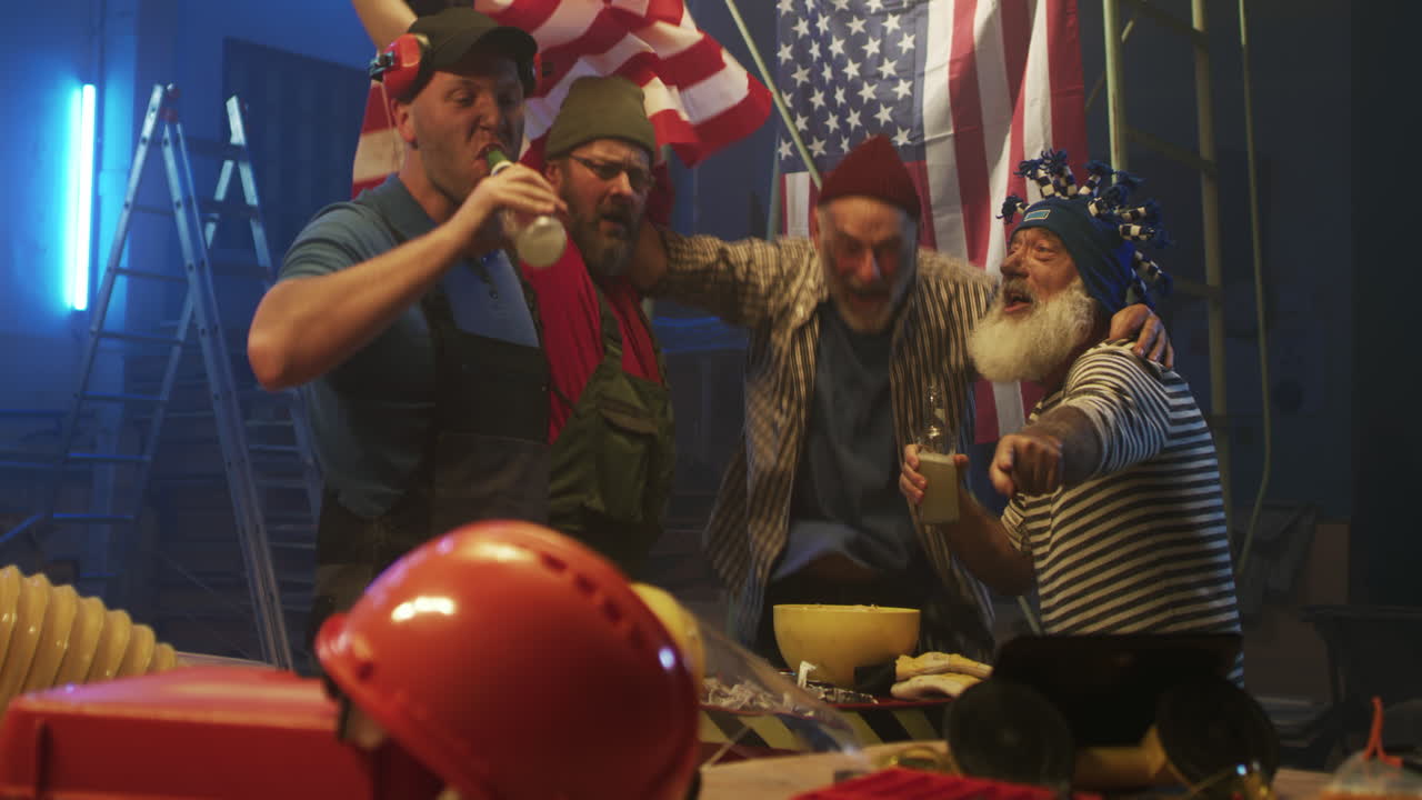 Group of enthusiastic American blue-collar workers celebrating with beer and flags in a workshop