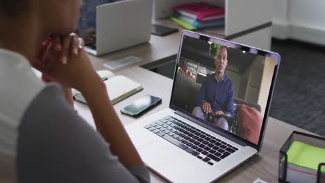 sección media de una mujer afroamericana haciendo una videollamada con un colega masculino en una computadora portátil en la oficina