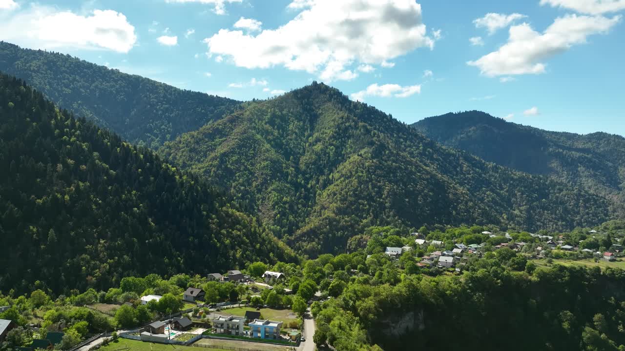 Drone shot overlooking a Georgian mountain village surrounded by green hills and valleys, with clear skies and soft sunlight enhancing the view